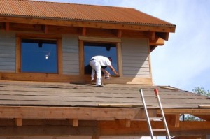 One worker puts stain on the trim of a second story window.