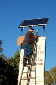 Jim Purvis, Local Electrician, Removes The Covering From The Solar Panel Above The Basic Necessities Sign In Nellysford, Virginia
