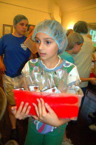 A youngster serves as a runner taking packaged meals to the next table for sealing before being boxed up for shipment around the world.