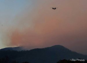 Photo courtesy of Debbie Wilson - Lukay Photography - Piney River, VA : Smoke rises in the background as a large forestry helicopter climbs across the area to dump water on the blaze at the Mount Pleasant wildfire in Amherst County, Virginia